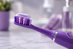 a close up image of an electric toothbrush in purple, with hydroxyapetite toothpaste on the brush head
